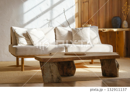 Modern minimalist interior of living room with beige sofa, rustic wooden table in natural sunlight Modern minimalist interior of living room with beige sofa, rustic wooden table in natural sunlight 132911137