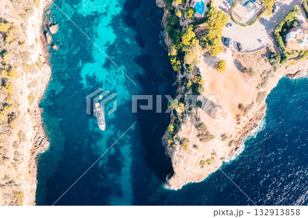 Yacht anchored in turquoise waters near a cliffside villa and historic tower in Majorca 132913858