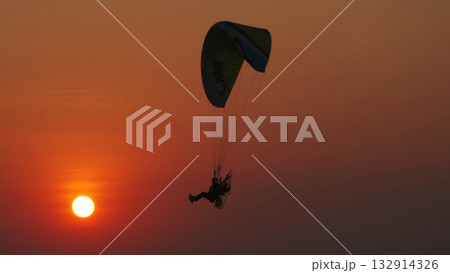 Motor paraglider flying through colorful sunset sky Motor paraglider flying through colorful sunset sky 132914326