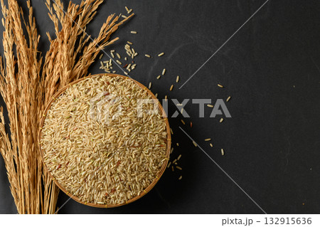 Top view of a round, traditional woven basket filled with uncooked brown rice grains. 132915636
