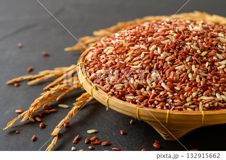 Close up of organic brown rice grains in a bamboo basket with golden rice stalks on black stone background. Close up of organic brown rice grains in a bamboo basket with golden rice stalks on black stone background. 132915662
