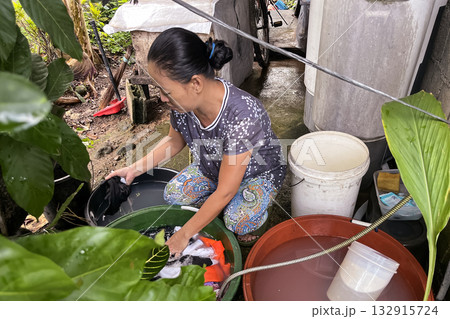An Asian woman washes clothes by hand in a basin An Asian woman washes clothes by hand in a basin 132915724