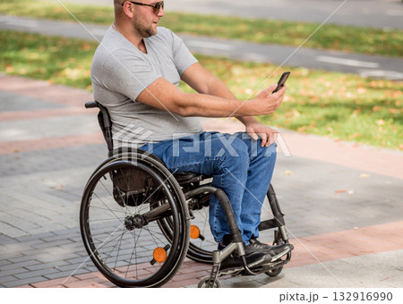 Handicapped man in wheelchair at the park alley use a smartphone 132916990