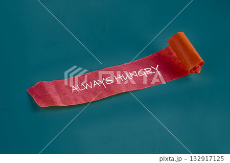 A vibrant piece of textured paper rolls out across a solid blue background, showcasing the bold phrase always hungry in playful handwriting. The warm colors invite curiosity and creativity A vibrant piece of textured paper rolls out across a solid blue background, showcasing the bold phrase always hungry in playful handwriting. The warm colors invite curiosity and creativity 132917125