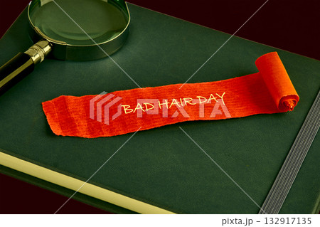 A colorful orange strip labeled BAD HAIR DAY rests on a dark green notebook beside a magnifying glass. The scene captures a lighthearted moment in an office or study setting A colorful orange strip labeled BAD HAIR DAY rests on a dark green notebook beside a magnifying glass. The scene captures a lighthearted moment in an office or study setting 132917135