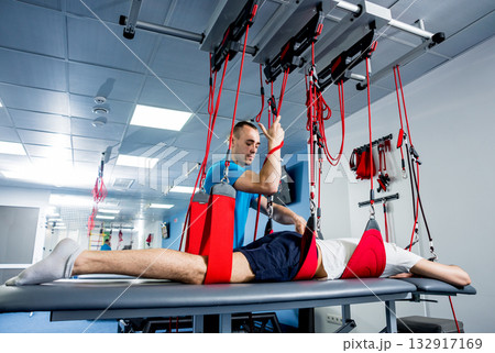 Physiotherapy. Suspension training therapy. Young man doing fitness traction Physiotherapy. Suspension training therapy. Young man doing fitness traction 132917169