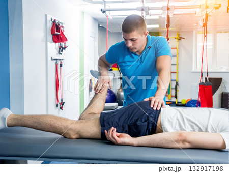 Rehabilitation therapy. Physiotherapist working with young male patient Rehabilitation therapy. Physiotherapist working with young male patient 132917198