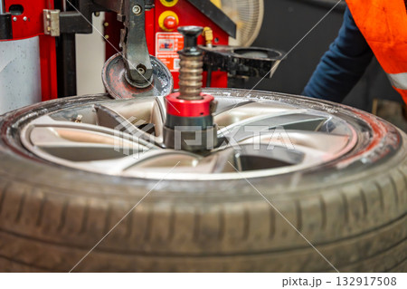 Tire changing machine removing the rubber tire from the rim using a rotating metal arm. Essential step in seasonal wheel replacement at a professional auto workshop. 132917508