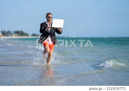 Business man in suit running with laptop at sea. successful business man enjoy summer. business man on summer vacation. business success of man. Beach meetings and conferences Business man in suit running with laptop at sea. successful business man enjoy summer. business man on summer vacation. business success of man. Beach meetings and conferences 132919772