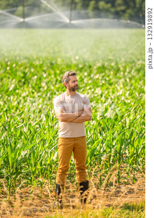 Man at irrigation system watering agricultural field. Farmer man countryside. Water sprinkler irrigating crop field. Drip irrigation system. Crop irrigation. Agriculture and farming. Soil fertility 132919892