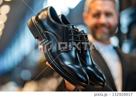 Business man choose elegant footwear in shop. Classic leather shoes for formal look. Formal shoe selective focus. Leather footwear. Shop assistant man in shoe store hold classic footwear. Shoe store 132920017