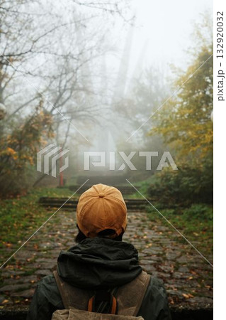 A lone traveler stands before the misty Kosmaj Monument, capturing the mood of solitude and exploration in a foggy autumn forest. Rear view. Serbia country 132920032