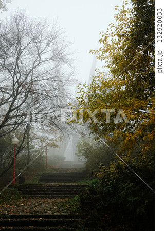 Mysterious view of the Kosmaj Monument rising through dense fog, surrounded by autumn trees and quiet forest atmosphere 132920033
