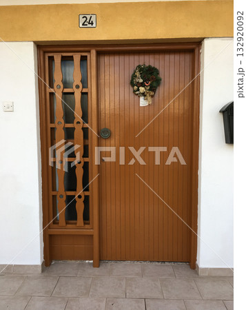 Brown wooden door with Christmas wreath and number plate. Architecture, holiday decoration, and cozy Mediterranean lifestyle. 132920092