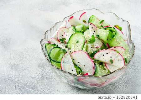 Fresh cucumber and radish salad served in a clear bowl with herbs on a light textured surface 132920541