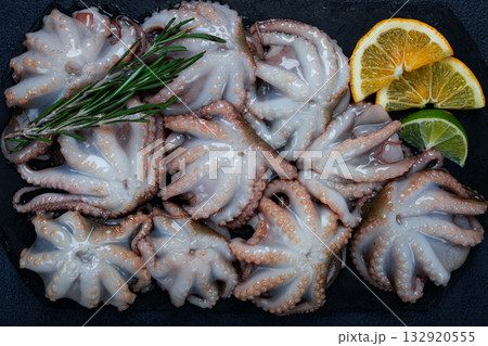 Fresh baby octopus, on black slate, with lemon and greenery, top view, no people, 132920555