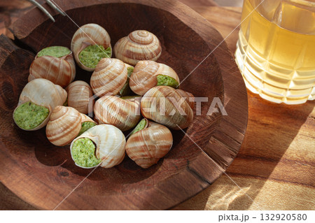 Snails cooked with herb oil on a wooden plate, served with white wine, natural light, no people, 132920580