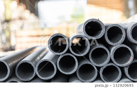 Stacked black pipes in industrial setting with blurred background elements 132920693