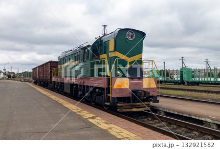 Powerful diesel locomotive hauls a heavy freight car. A freight train on the tracks, front view. Summer clouds loom Powerful diesel locomotive hauls a heavy freight car. A freight train on the tracks, front view. Summer clouds loom 132921582