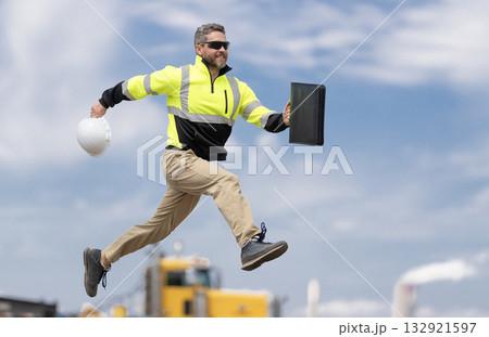 Man engineer running to success. Builder man run fast to work. Engineer supervisor running outdoor. Supervisor jumping. Excited builder construction worker jumping in front of trucks. Good job 132921597