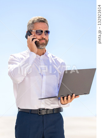 Remote working. Phone call communication. Businessman busy working on laptop outdoor. Man has business phone call. Successful businessman boss freelancing online. Business man working online Remote working. Phone call communication. Businessman busy working on laptop outdoor. Man has business phone call. Successful businessman boss freelancing online. Business man working online 132921614