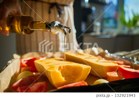 Woman pouring olive oil over pumpkin and vegetables in kitchen Woman pouring olive oil over pumpkin and vegetables in kitchen 132921943