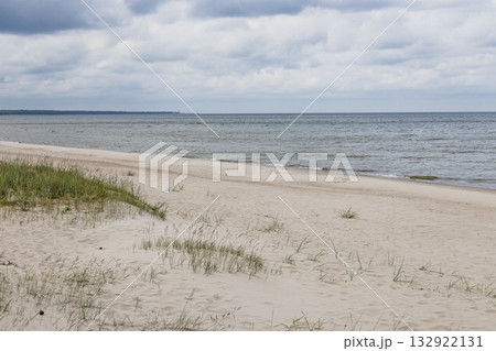 Baltic Sea sandy beach with dune grass and calm waves under a moody cloudy sky Baltic Sea sandy beach with dune grass and calm waves under a moody cloudy sky 132922131