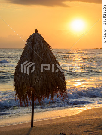 umbrella on the sand beach at sunrise. summer vacation at the sea. blue sky with glowing clouds. beautiful landscape for travel with sun above horizon. tranquil scenery in orange light 132922258