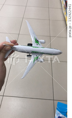 A hand holding a white toy airplane with green accents. Representation of childhood imagination, aviation fascination, and dreams of global travel. A hand holding a white toy airplane with green accents. Representation of childhood imagination, aviation fascination, and dreams of global travel. 132922441