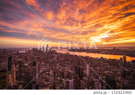 Aerial view of New York City at sunset with vibrant orange sky reflecting in the Hudson River and illuminated skyscrapers under dramatic clouds 132922460