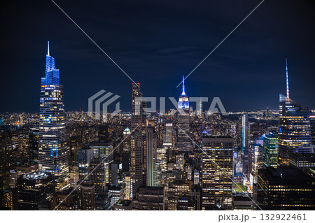 Night skyline of Manhattan with illuminated skyscrapers and the Empire State Building glowing in blue light Night skyline of Manhattan with illuminated skyscrapers and the Empire State Building glowing in blue light 132922461