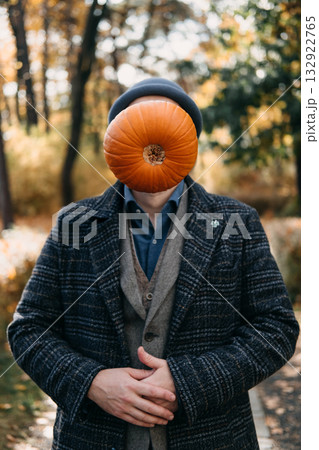 Man standing in a forest path with a pumpkin obscuring his face and wearing a dark hat. Visual metaphor, identity in digital age, anonymity, personal expression 132922765