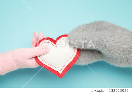 Female hands in warm mittens gives a heart children's hand in gloves on blue background 132923025