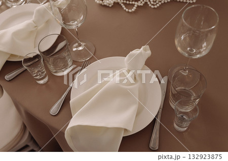 Elegant wedding table setting with white plates, napkins and floral centerpiece on beige tablecloth Elegant wedding table setting with white plates, napkins and floral centerpiece on beige tablecloth 132923875