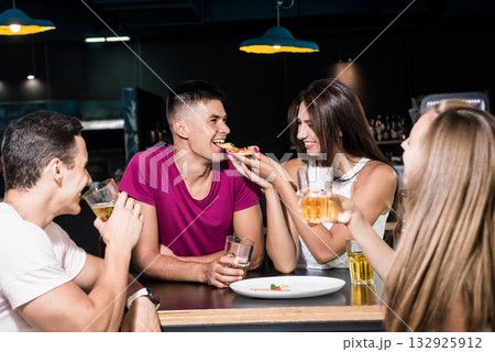 Cheerful friends in the pub. Drinking beer, eating pizza, talking, having fun. 132925912