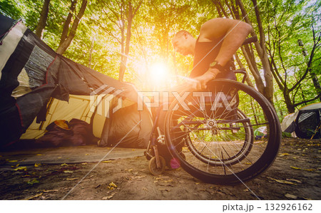 Disabled man resting in a campsite with friends. Wheelchair in the forest Disabled man resting in a campsite with friends. Wheelchair in the forest 132926162