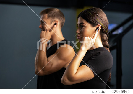 man and woman wear headphones as they listen to music. They focus on their workout demonstrating fitness and teamwork in their routine. man and woman wear headphones as they listen to music. They focus on their workout demonstrating fitness and teamwork in their routine. 132926960