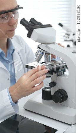 Female scientist wearing protective gear analyzing test samples under microscope in contemporary research environment. Medicine, healthcare and science concept Female scientist wearing protective gear analyzing test samples under microscope in contemporary research environment. Medicine, healthcare and science concept 132928180
