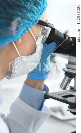 Female scientist in blue gloves and mask using microscope in laboratory setting, conducting important research and analysis, close-up. Medicine and science concept Female scientist in blue gloves and mask using microscope in laboratory setting, conducting important research and analysis, close-up. Medicine and science concept 132928320