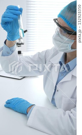 Medical science researcher wearing blue protective gear of cap, gloves and googles, is examining liquid in test tube in laboratory workspace. Medicine and health care concept Medical science researcher wearing blue protective gear of cap, gloves and googles, is examining liquid in test tube in laboratory workspace. Medicine and health care concept 132928350
