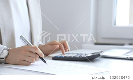 Businesswoman is calculating annual tax using calculator and taking notes in the office, managing domestic budget and checking financial documents. Audit and taxes in business Businesswoman is calculating annual tax using calculator and taking notes in the office, managing domestic budget and checking financial documents. Audit and taxes in business 132928476