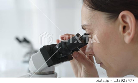 Female scientist peering into microscope, analyzing biological sample with precision in sterile laboratory research environment. Medicine and science concept Female scientist peering into microscope, analyzing biological sample with precision in sterile laboratory research environment. Medicine and science concept 132928477