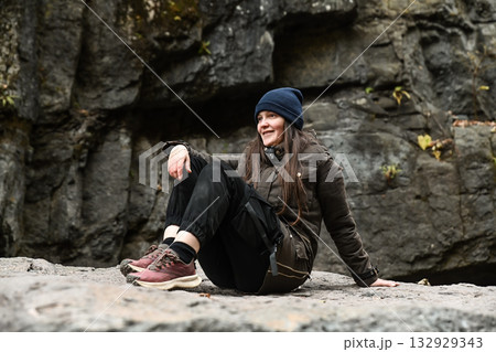 Russian woman traveler sitting on a rock near a waterfall. Autumn hike adventure in the mountains, enjoying nature and outdoor freedom. Russian woman traveler sitting on a rock near a waterfall. Autumn hike adventure in the mountains, enjoying nature and outdoor freedom. 132929343
