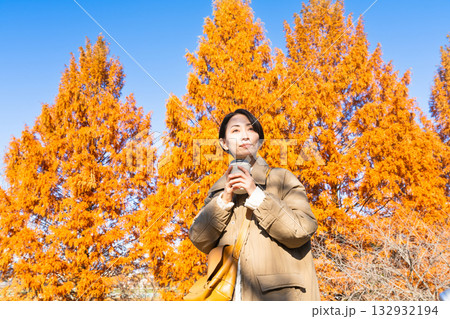 紅葉を楽しみながらホットドリンクを飲む女性　ライフスタイルイメージ 132932194