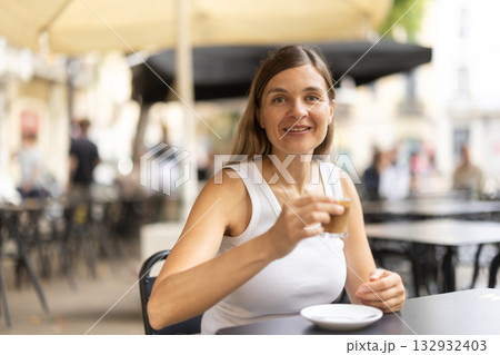 On summer outside of cafe, woman is relaxing at table, drinking coffee On summer outside of cafe, woman is relaxing at table, drinking coffee 132932403