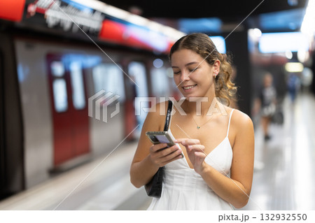 Young girl standing on metro platform with phone in hand Young girl standing on metro platform with phone in hand 132932550