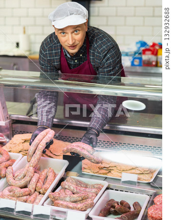 Confident male butcher holding large beef sausage in meat section of supermarket 132932688