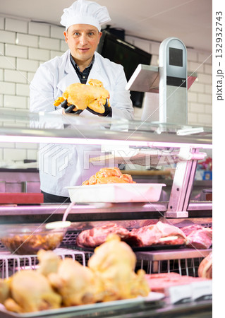 Confident male butcher offering to sell whole chicken in butcher shop Confident male butcher offering to sell whole chicken in butcher shop 132932743