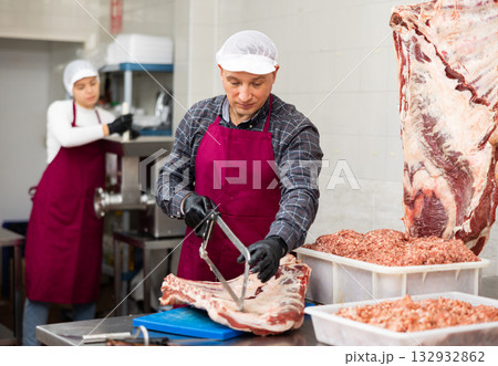 Happy female butcher sawing big chunk of beef meat in meat section of supermarket 132932862