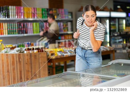Young girl looks and chooses frozen food in refrigerator in supermarket 132932869